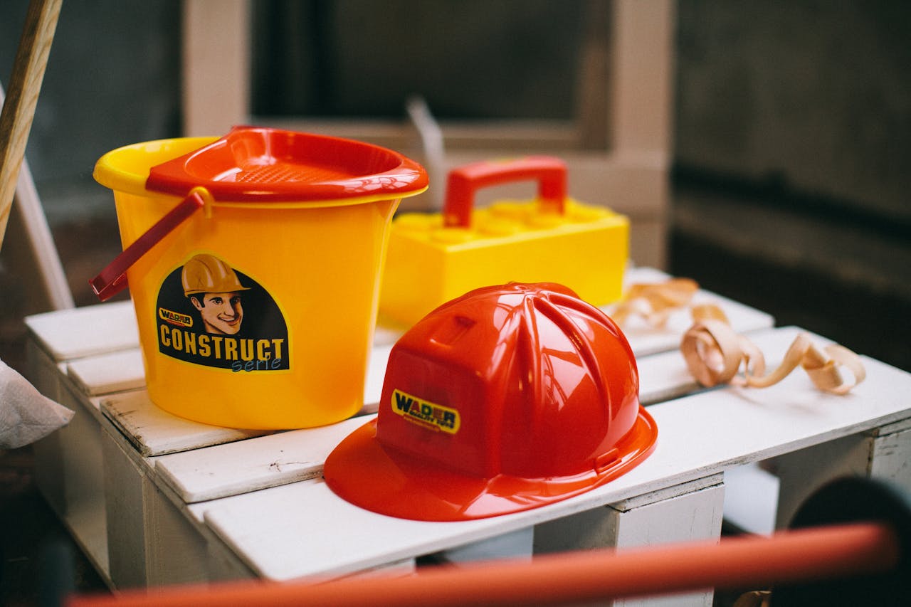 Bright toy construction set with hard hat, bucket, and toolbox on a wooden crate.